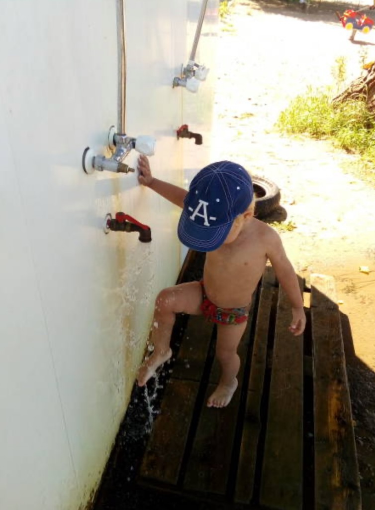 A child rinsing off under an outdoor shower after swimming.