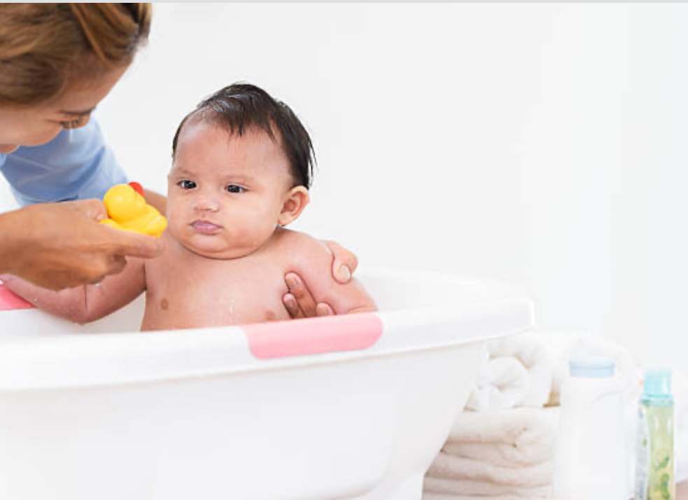 A smiling parent gently holding a newborn in a shallow baby bathtub, surrounded by soft towels and bath essentials